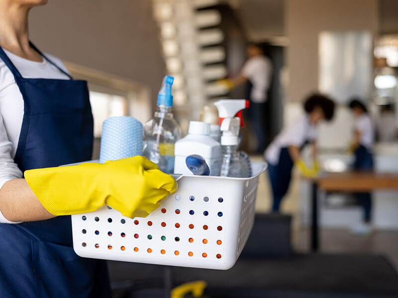 worker holding basket of cleaning supplies in home