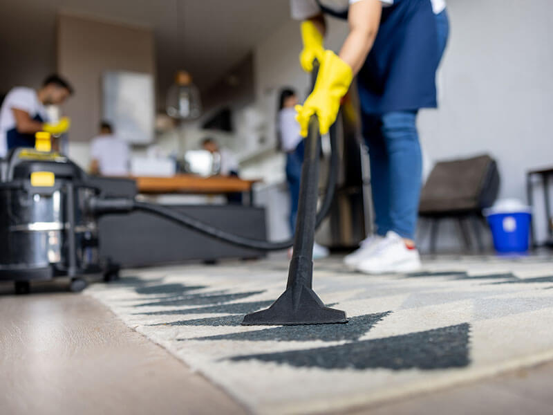 worker vacuuming carpet in home