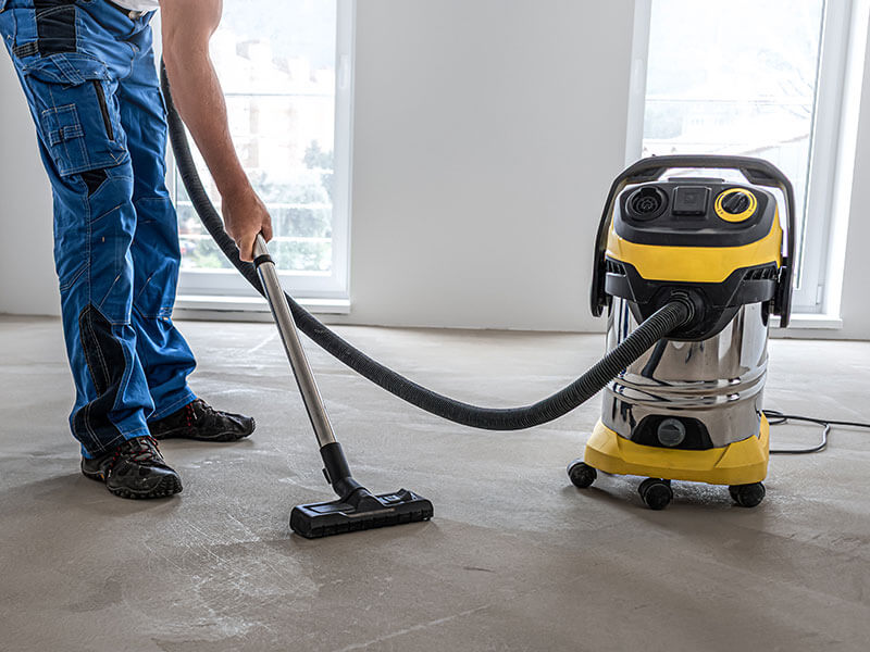 worker vacuuming bare floor during construction